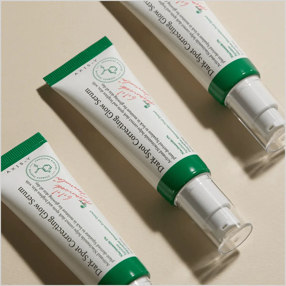 Two tubes of 'Dark Spot Correcting Glow Serum' with green and white packaging on a beige background.