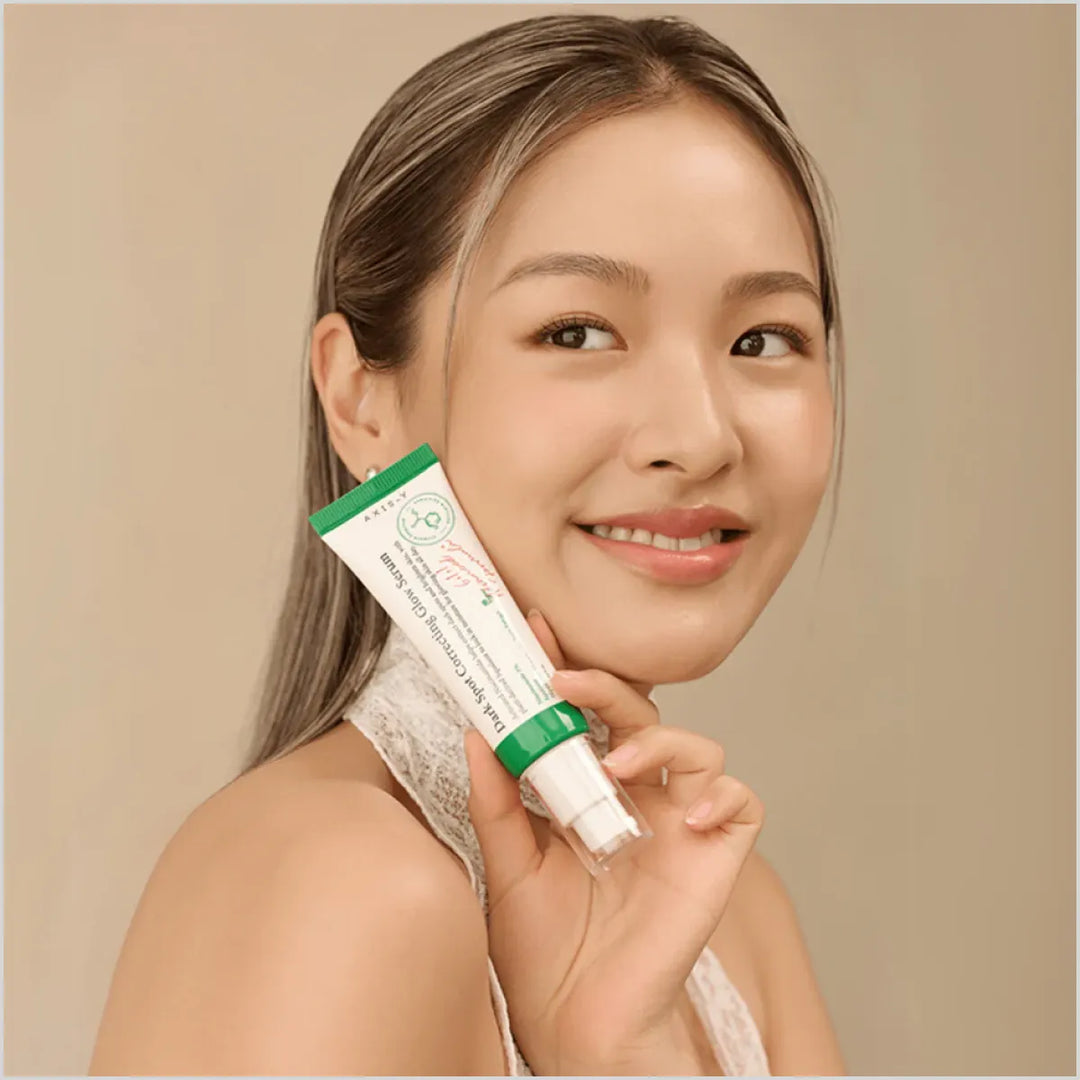 Woman holding a tube of cream against her face on a beige background